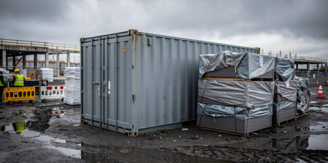 Chantier immobilier sous ciel couvert, avec un conteneur de stockage sécurisé et des matériaux protégés par des bâches.